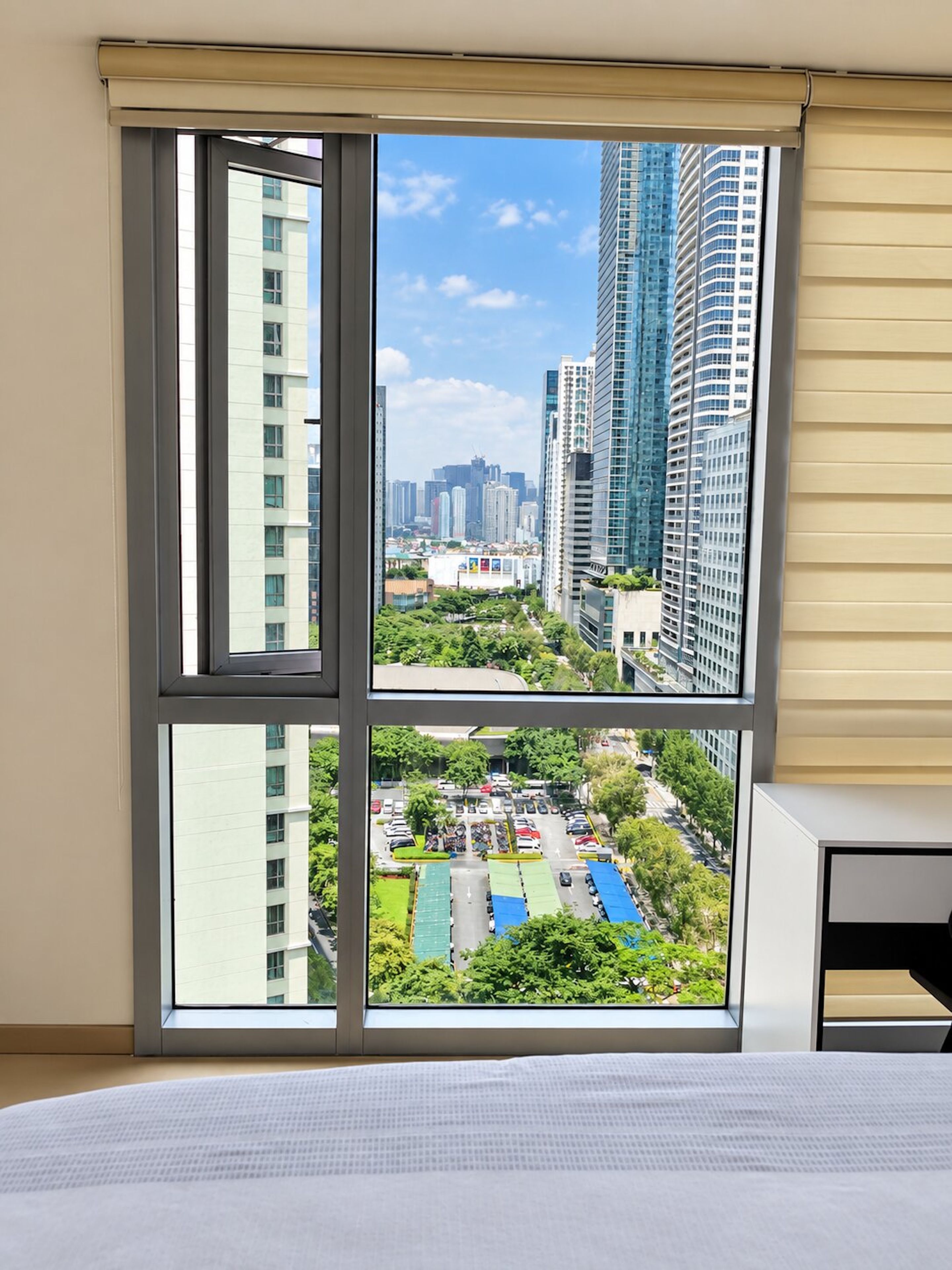 A room with a large window offering a view of a cityscape, including high-rise buildings and a parking area.