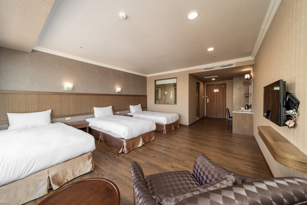 Una habitación de hotel con tres camas, un escritorio, una silla y un televisor.