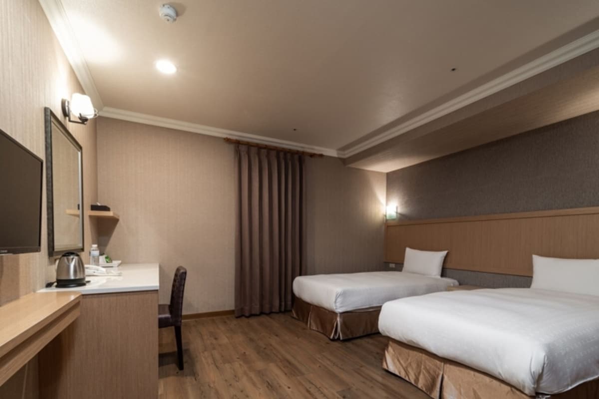 Habitación de hotel con dos camas, un escritorio, una silla, un televisor de pantalla plana y un espejo.