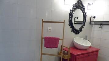 Ett badrum med vita, kaklade väggar, ett trähandduksställ med en rosa handduk, en vit tvättställ placerad på en röd bänkskiva och en svart, utsmyckad spegel.