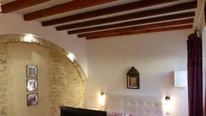 Une chambre avec un mur en pierre, un lit avec une literie à motifs floraux, une télévision et une petite table.