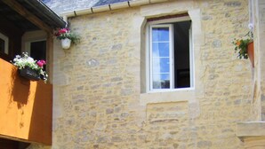 Un bâtiment en pierre avec un banc en bois, deux fenêtres ornées de jardinières et une porte.