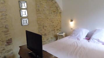 Een slaapkamer met een stenen muur, een bed met witte lakens, een nachtkastje met een afstandsbediening en een flatscreen televisie op een houten dressoir.