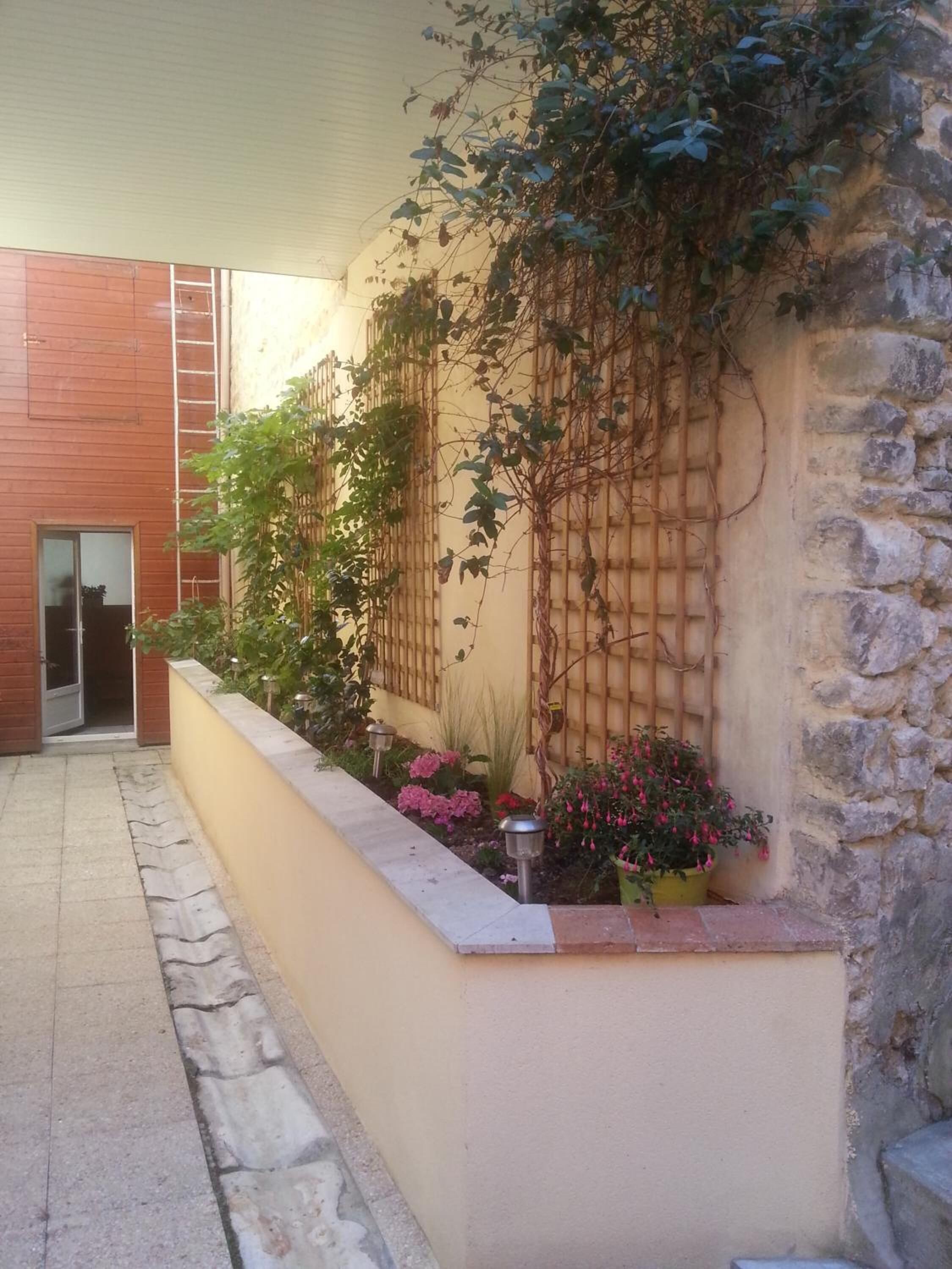 A courtyard with a stone wall, a wooden fence, and potted plants.