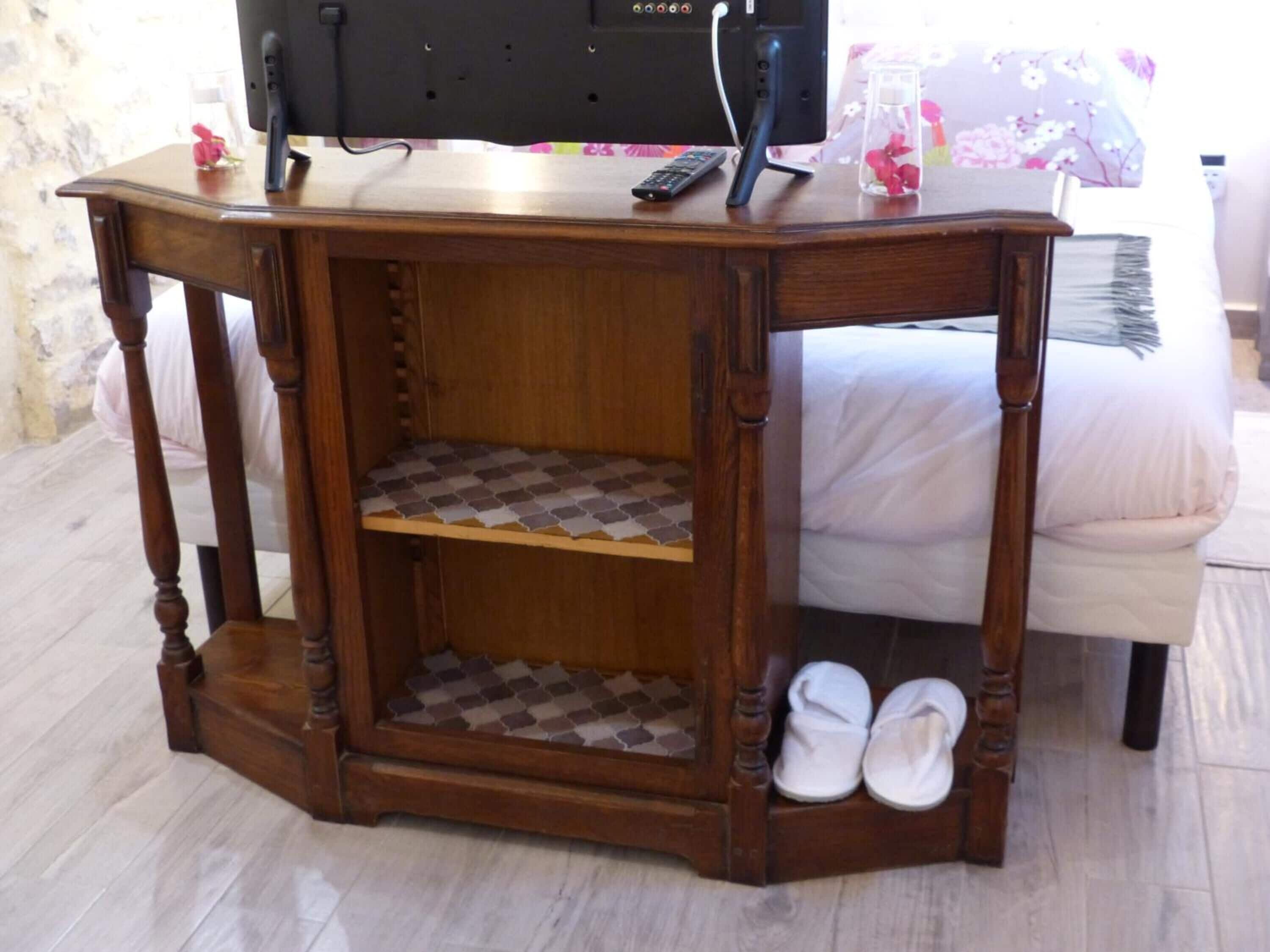 Une table de chevet en bois, avec une étagère, une télécommande et un vase rempli de fleurs.