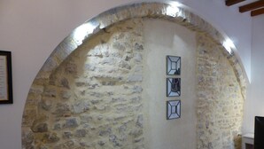 Un mur en pierre avec une porte en bois, un miroir encadré et un téléviseur posé sur un meuble en bois.