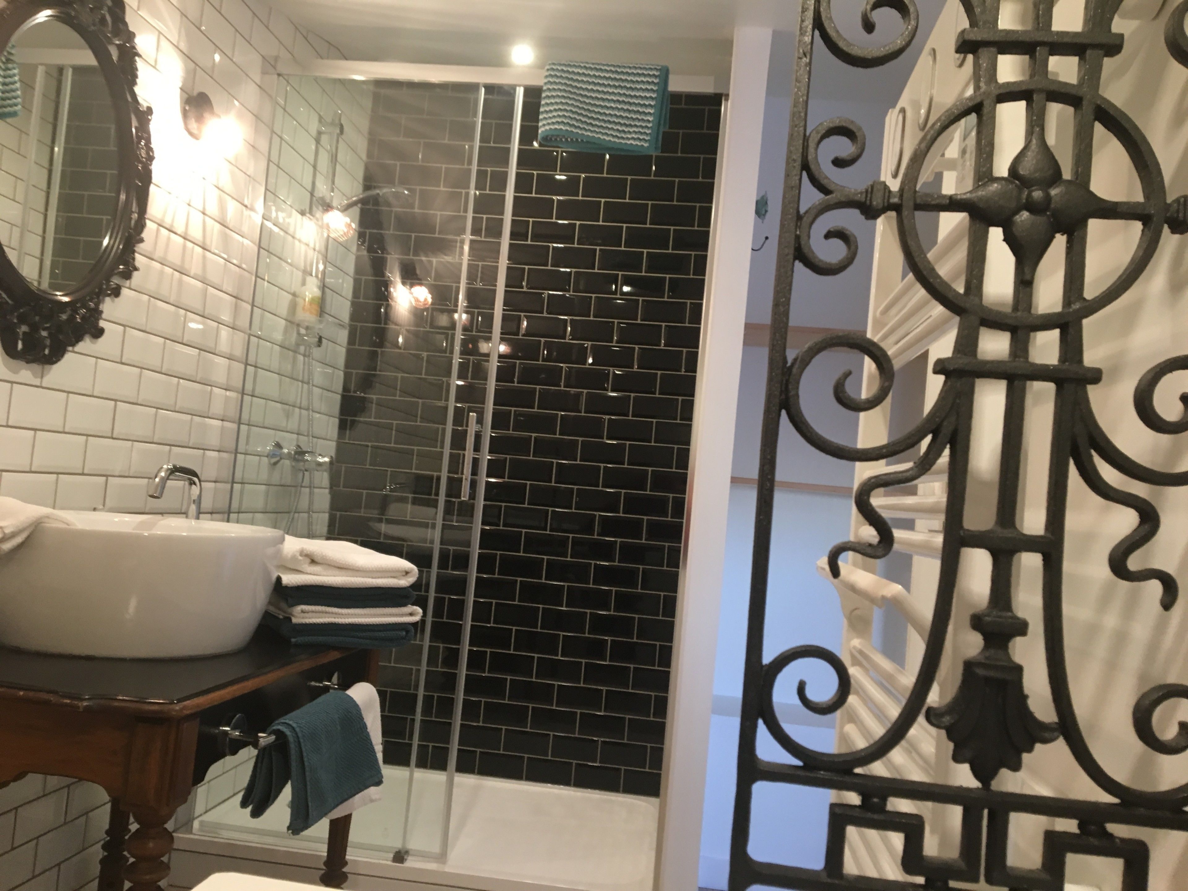 A bathroom with a white sink, a mirror, and a shower area with black tiles.