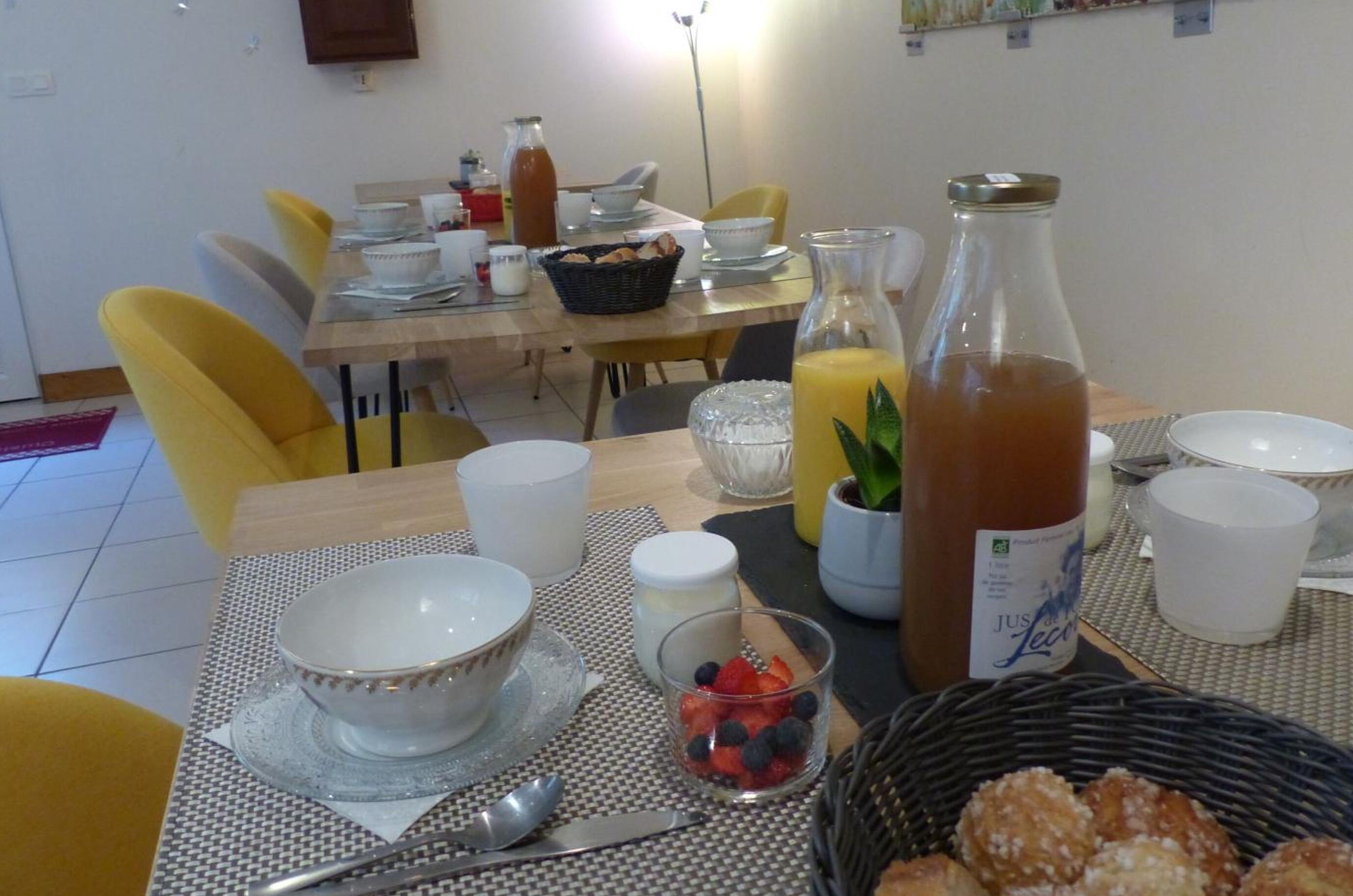 Un desayuno servido en una mesa con sillas, que incluye tazones, vasos, una botella de jugo y una cesta de pasteles.