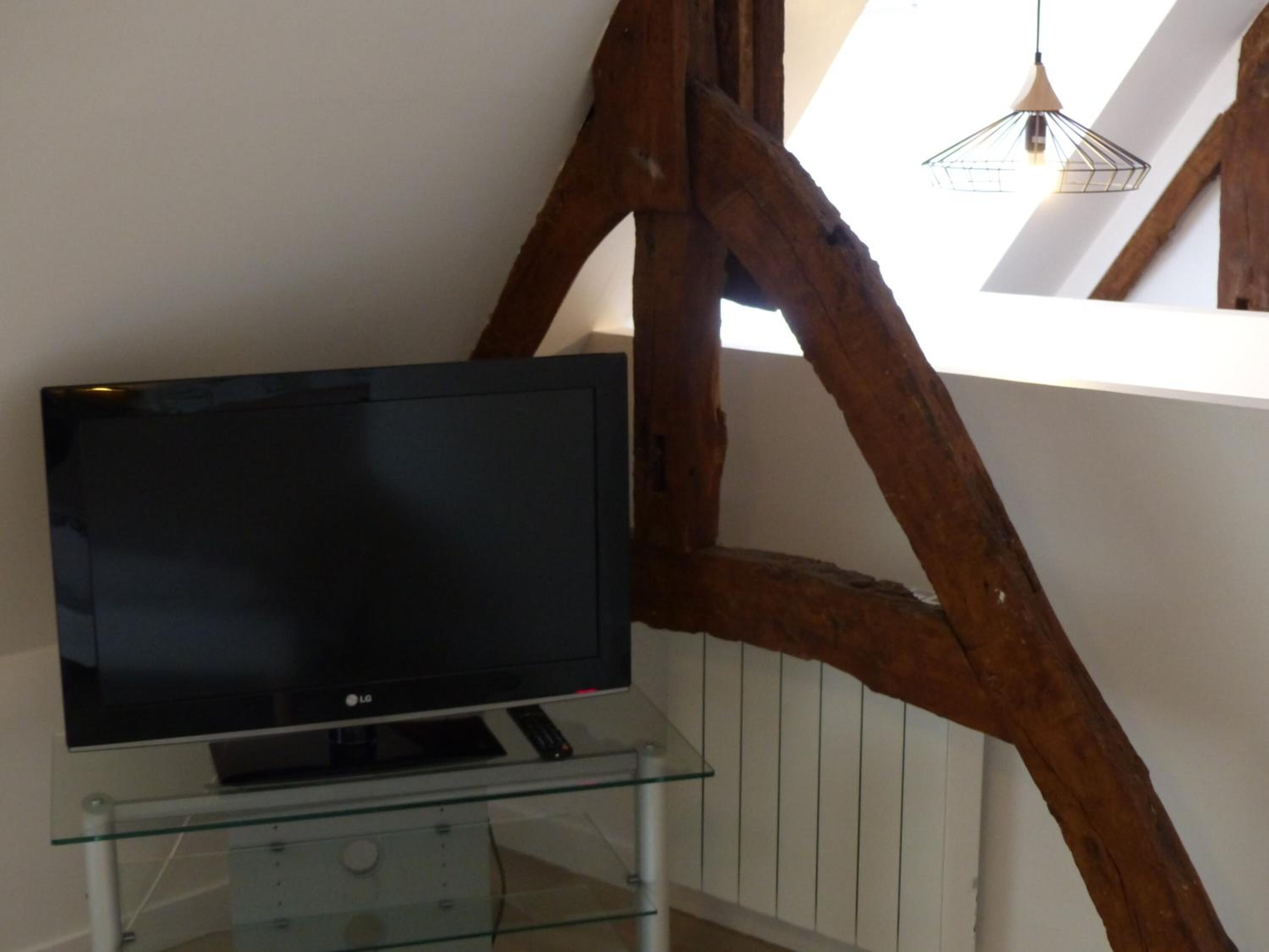 Un televisor de pantalla plana sobre un estante de vidrio en una habitación con vigas de madera a la vista y una pared blanca.