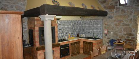 A rustic kitchen with a stone wall, a tiled backsplash, and wooden cabinets.