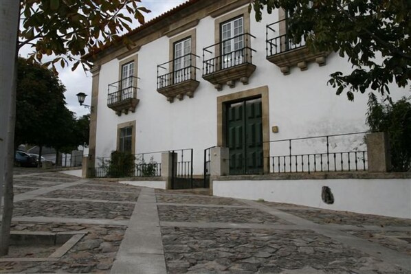 A building with a white facade, multiple windows, and a green door. There are stone steps leading up to the entrance, and a metal fence surrounds the property.