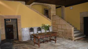 Um quarto com piso de pedra, uma mesa de madeira, um vaso de flores e parede com azulejos.