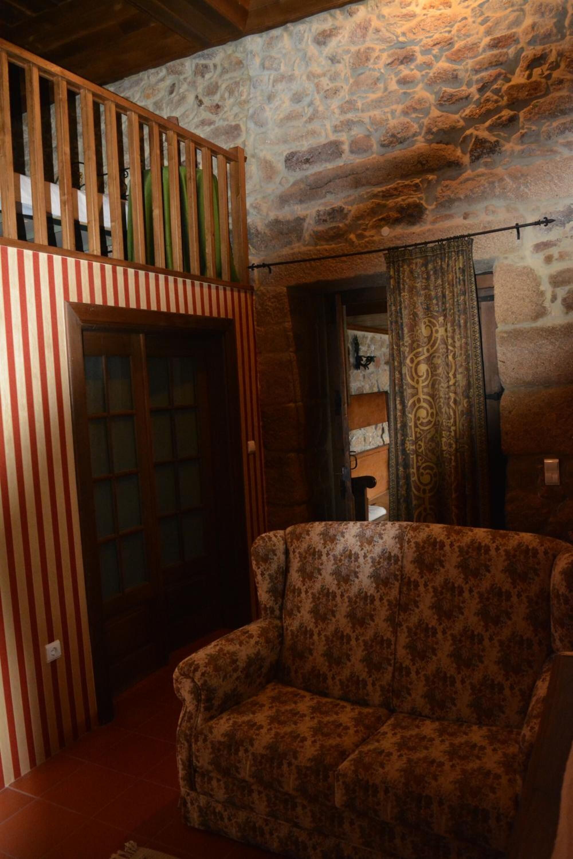 Een rustieke kamer met een stenen muur, een houten bank en een fauteuil met een patroon.