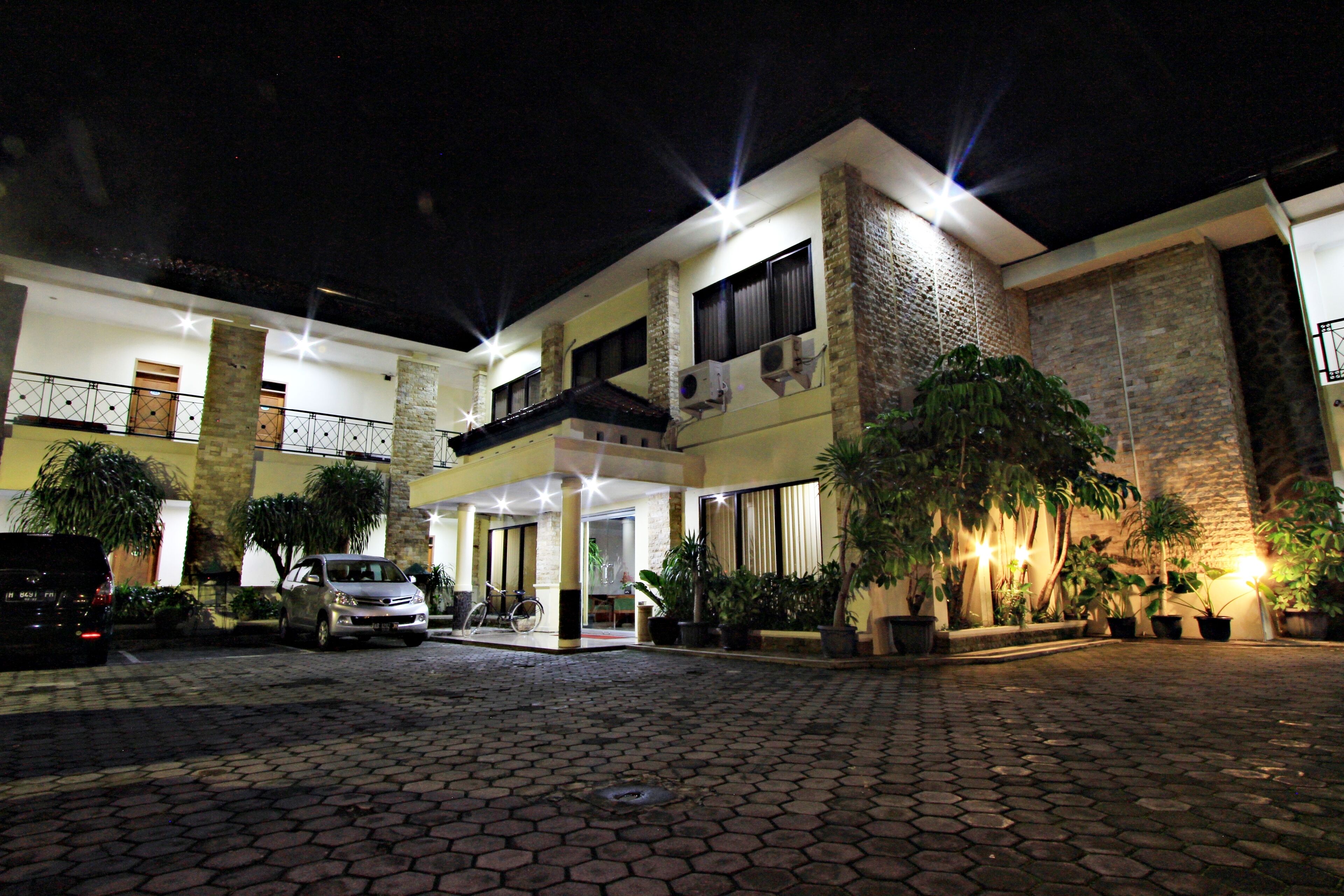 A multi-story building with a courtyard, featuring a car parked in front, potted plants, and a bicycle.