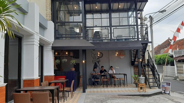 An outdoor café with tables and chairs, a staircase, and a mural on the wall. - Griya Sentana Hotel Jogjakarta (Yogyakarta)