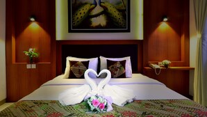 A hotel room with a bed, two wall-mounted lamps, a painting of peacocks, and a bouquet of flowers. - Griya Sentana Hotel Jogjakarta (Yogyakarta)