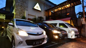A building with a stone facade and a triangular logo. There are three cars parked in front. - Griya Sentana Hotel Jogjakarta (Yogyakarta)