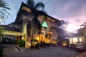 A hotel with a prominent green logo, a tiled entrance, and a bicycle parked outside. - Griya Sentana Hotel Jogjakarta (Yogyakarta)