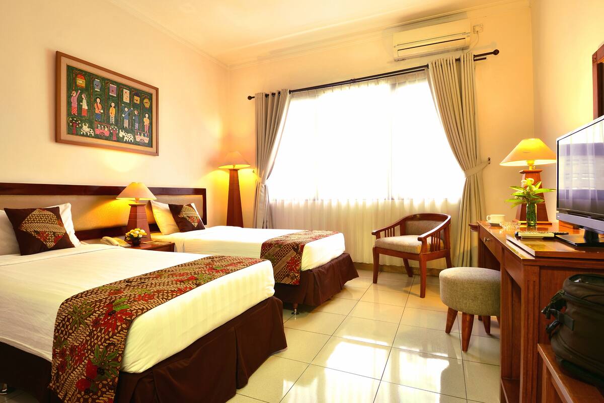 A hotel room with two beds, a desk with a television, a chair, and a large window with curtains.