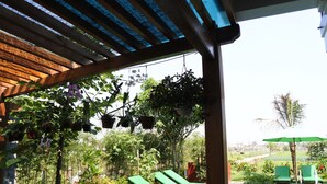 A covered outdoor area with a pool, green lounge chairs, and hanging planters. - Hoi An Osaka Riverside Villa & Spa (Da Nang)