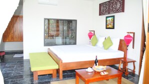 A hotel room with a bed, a bench, a table with a bottle and a basket, a window, and a decorative panel. - Hoi An Osaka Riverside Villa & Spa (Da Nang)