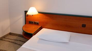 A hotel room with a wooden headboard, a bedside table with a lamp, and a neatly made bed with a white pillow.