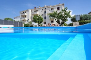 A swimming pool with a clear blue water surface, surrounded by a building with balconies and trees. - Hotel Mediteran (Zadar)