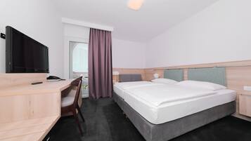 Een hotelkamer met een bed, bureau, stoel, televisie en raam met gordijnen.
