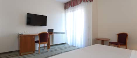 A hotel room with a bed, a desk with a chair, a television, and a window with curtains.