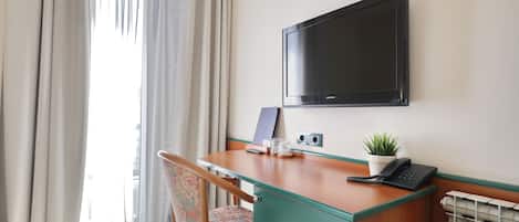 Habitación de hotel con un escritorio de madera, un televisor de pantalla plana, un teléfono, una planta y un radiador.