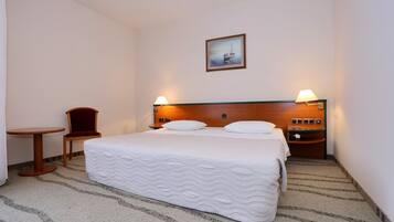 A hotel room with a bed, a chair, a small table, and a nightstand with a lamp.