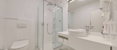 A modern bathroom with a glass shower enclosure, a toilet, a sink, and a hairdryer.