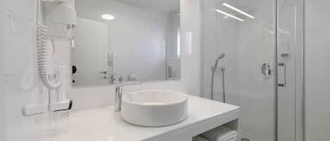 A modern bathroom with a white sink, a glass shower enclosure, and a hairdryer mounted on the wall.