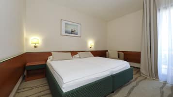 A hotel room with a bed, two wall-mounted lamps, a painting, and a window with curtains.