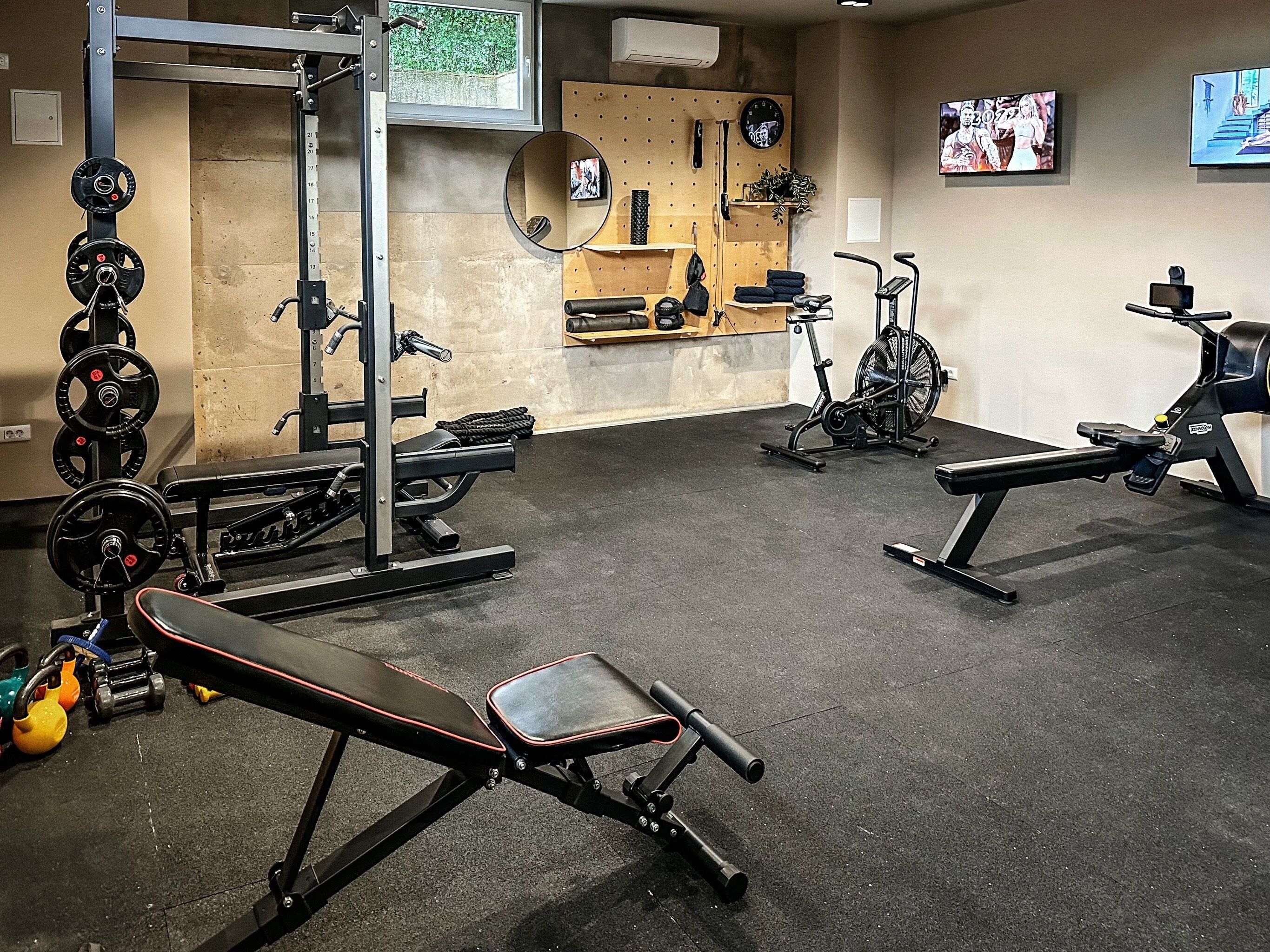 Un gimnasio con equipo de levantamiento de pesas, máquinas de cardio y bancos.