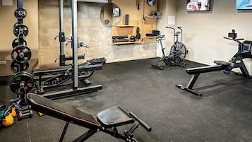 Un gimnasio con equipo de levantamiento de pesas, máquinas de cardio y bancos.