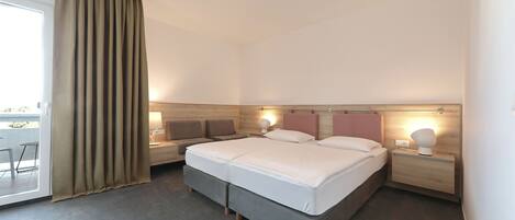 Una habitación de hotel moderna con una cama grande, dos mesitas de noche con lámparas, una puerta de cristal corredera y vistas al exterior.