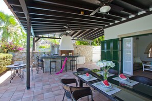 Une terrasse extérieure équipée d’un barbecue, d’une table à manger, de chaises et d’un mur en pierre.