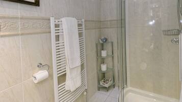Een moderne badkamer met een douchecabine van glas, een witte badkuip, toilet en een handdoekhouder.