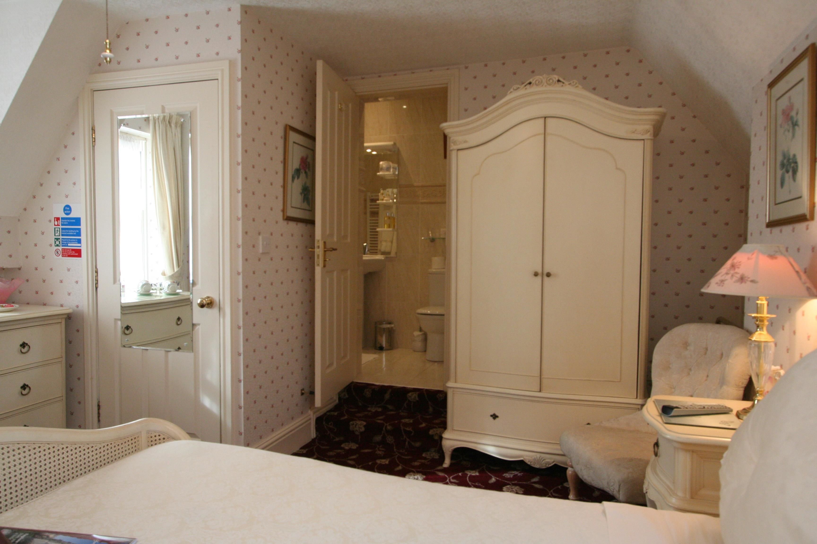 A bedroom with a bed, a wardrobe, a chair, and a bedside table with a lamp.