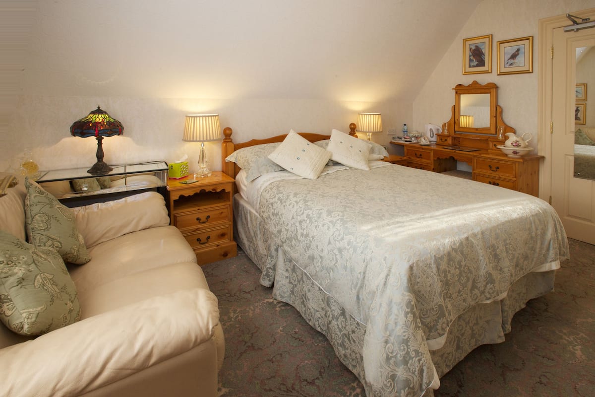 A bedroom with a bed, a nightstand, a dresser, a lamp, and a mirror.