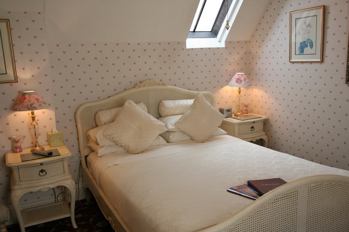 A bedroom with a bed, two bedside tables, a nightstand, a window, and a wall with floral wallpaper.