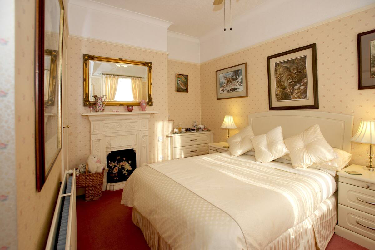A bedroom with a large bed, a dresser, a nightstand, a mirror, and a fireplace.