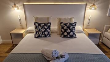 Una cama bien hecha con dos almohadones estampados, dos mesitas de noche y dos lámparas de pared.