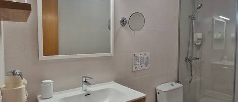 Un baño moderno con tocador de madera, un espejo grande, ducha e inodoro con ducha.