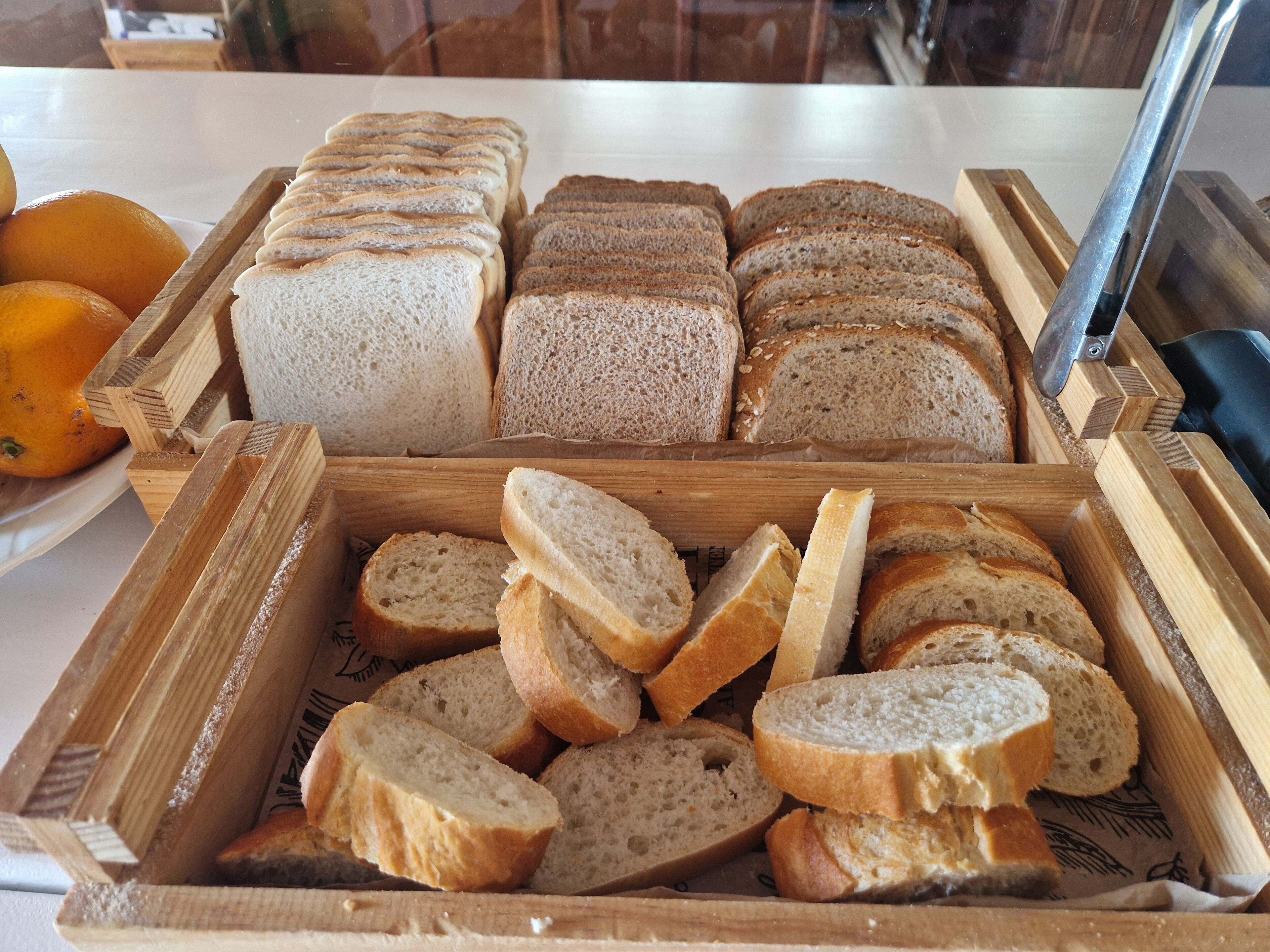 A variety of sliced breads in wooden containers, with a knife and oranges visible.