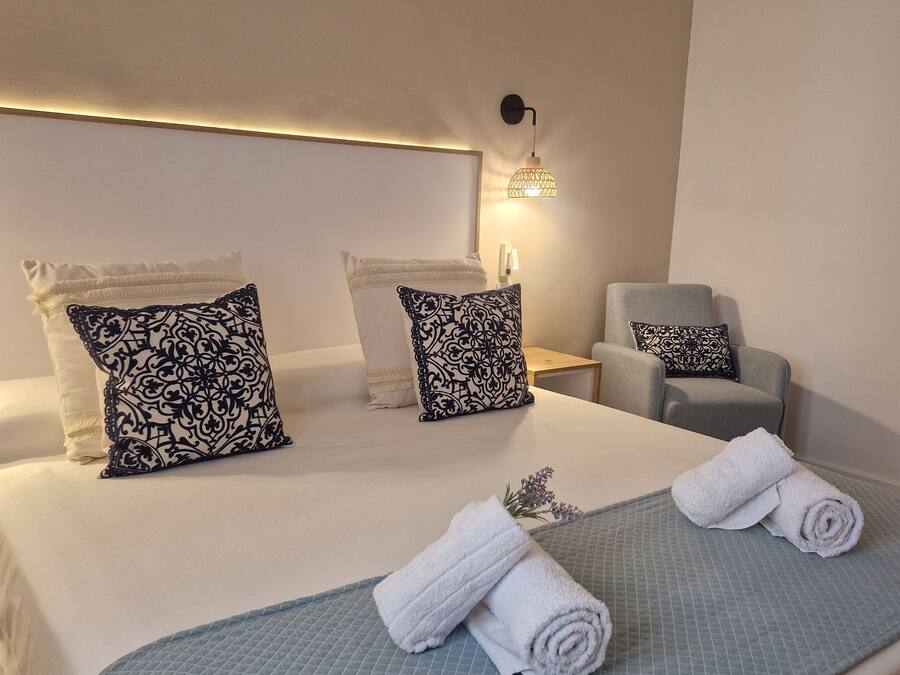 A hotel room with a large bed, two bedside tables, a chair, and a wall-mounted lamp.
