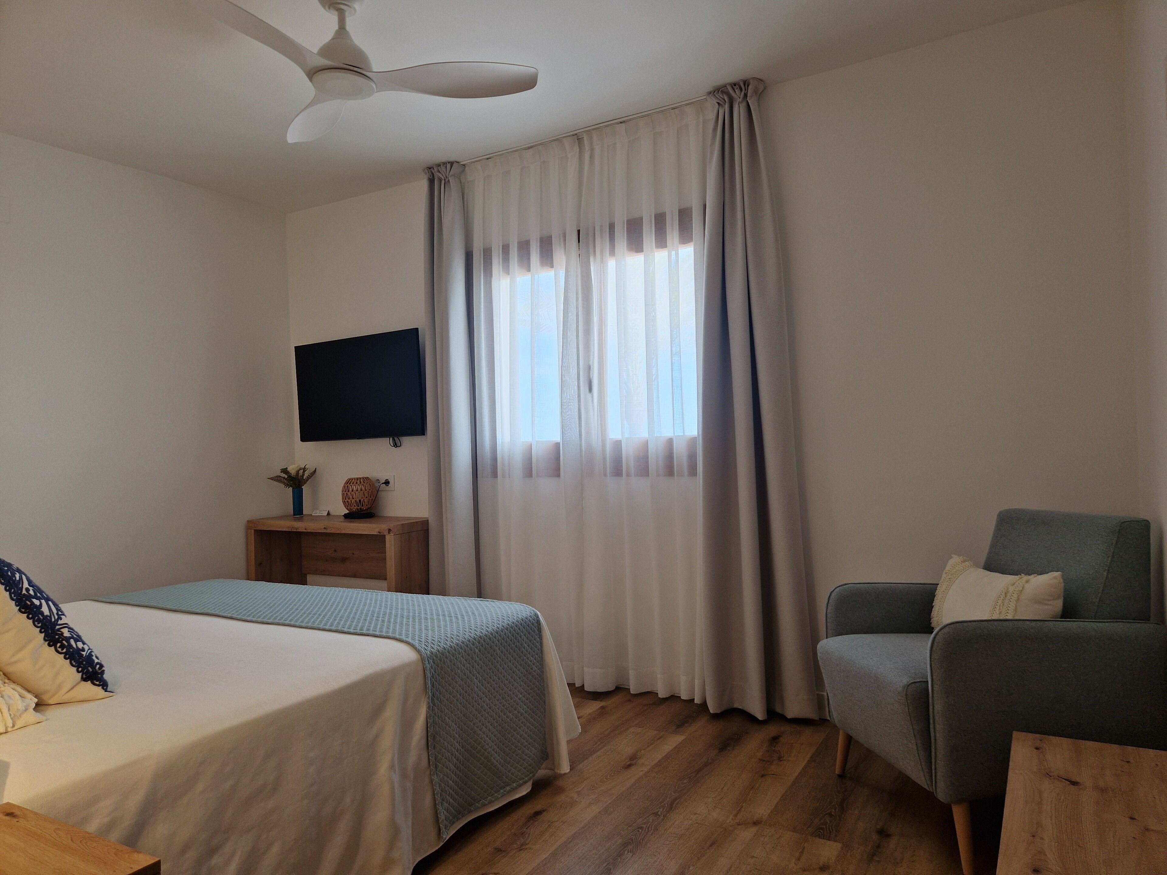 A hotel room with a bed, a chair, a TV on the wall, and a window with curtains.