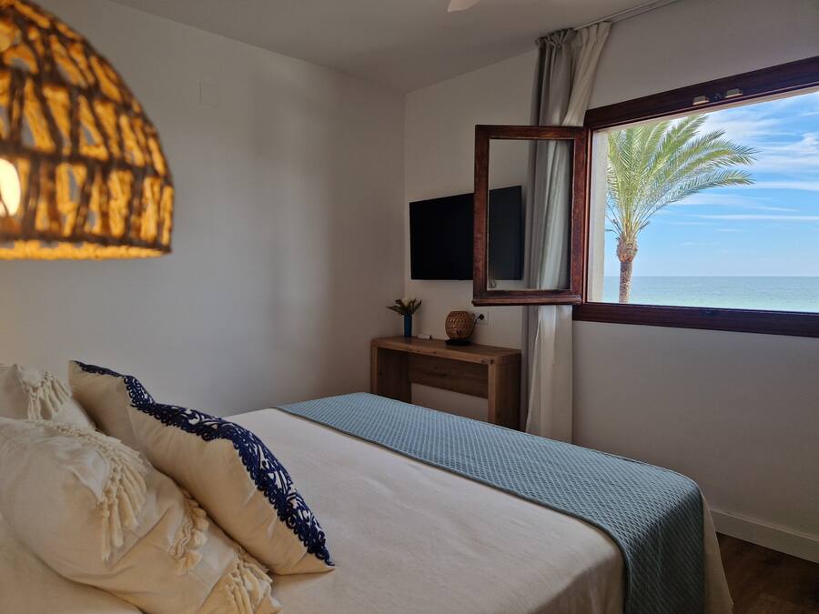 Een slaapkamer met een bed, nachtkastje, spiegel en uitzicht op zee.