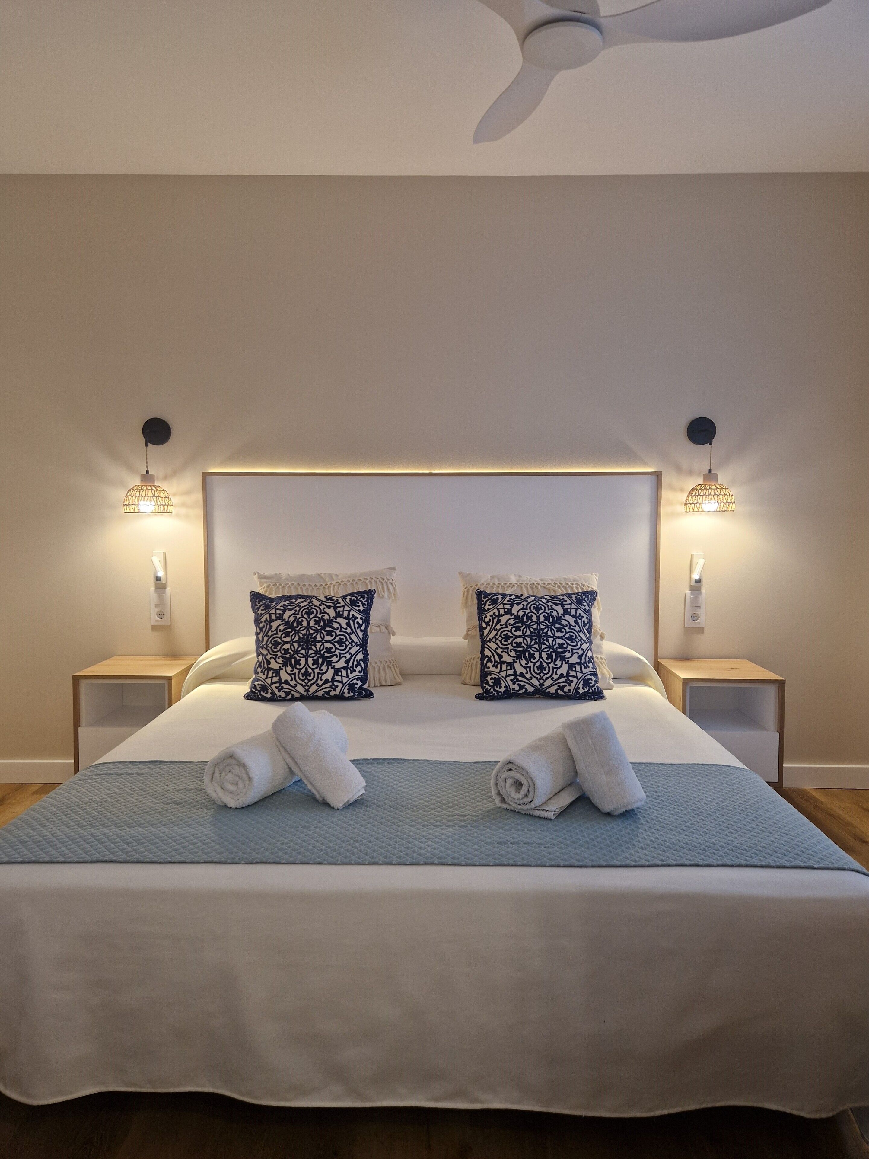 A neatly made bed with two decorative pillows, a bedside table with a lamp, and a ceiling fan.
